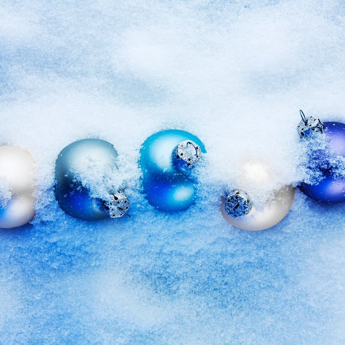 Blue and apricot-coloured Christmas baubles hidden in the snow
