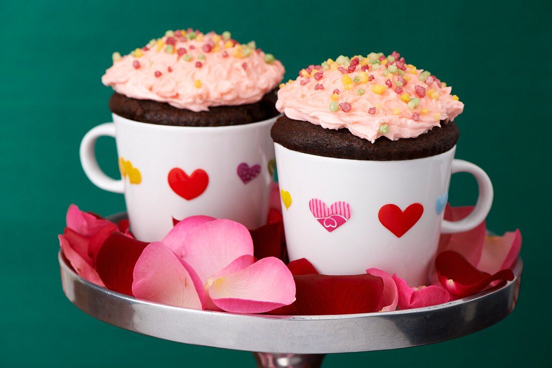 Schoko-Cupcakes in Kaffeetassen mit Stickerherzen und Rosenblütenblättern