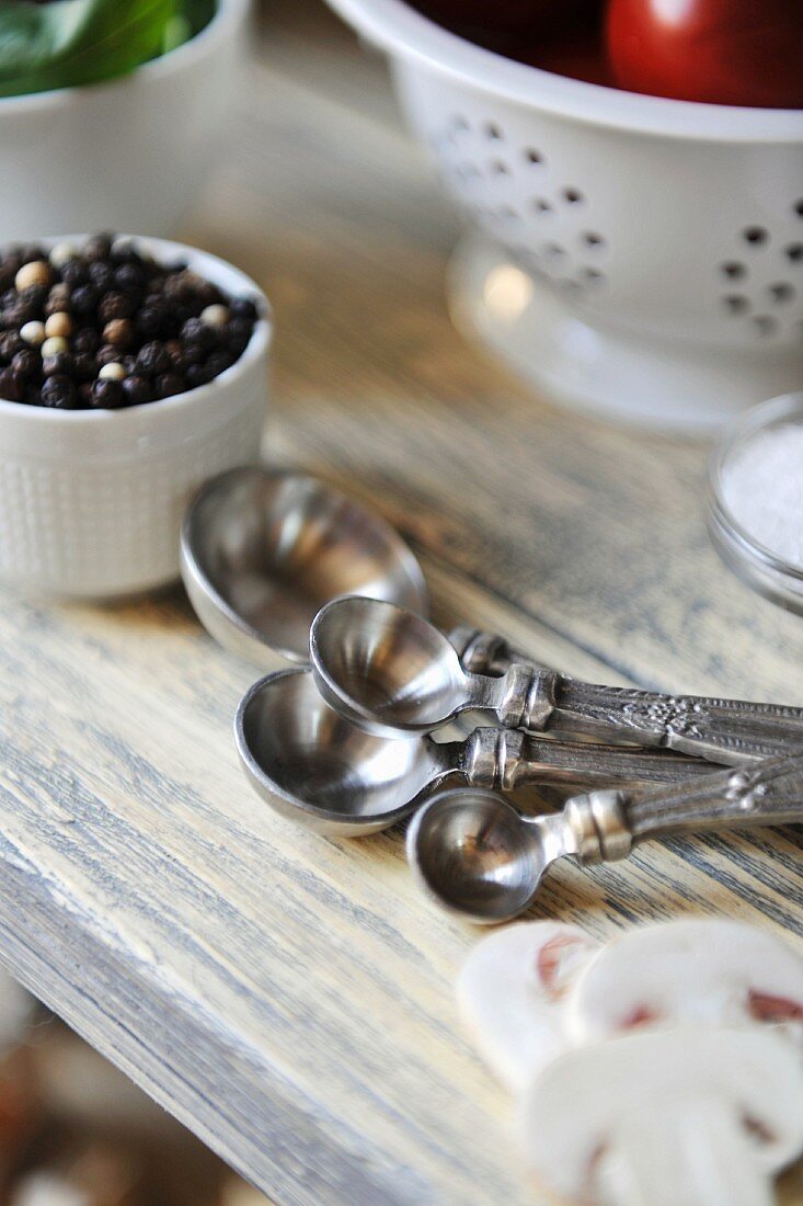 Assorted silver measuring spoons, peppercorns and sliced mushrooms