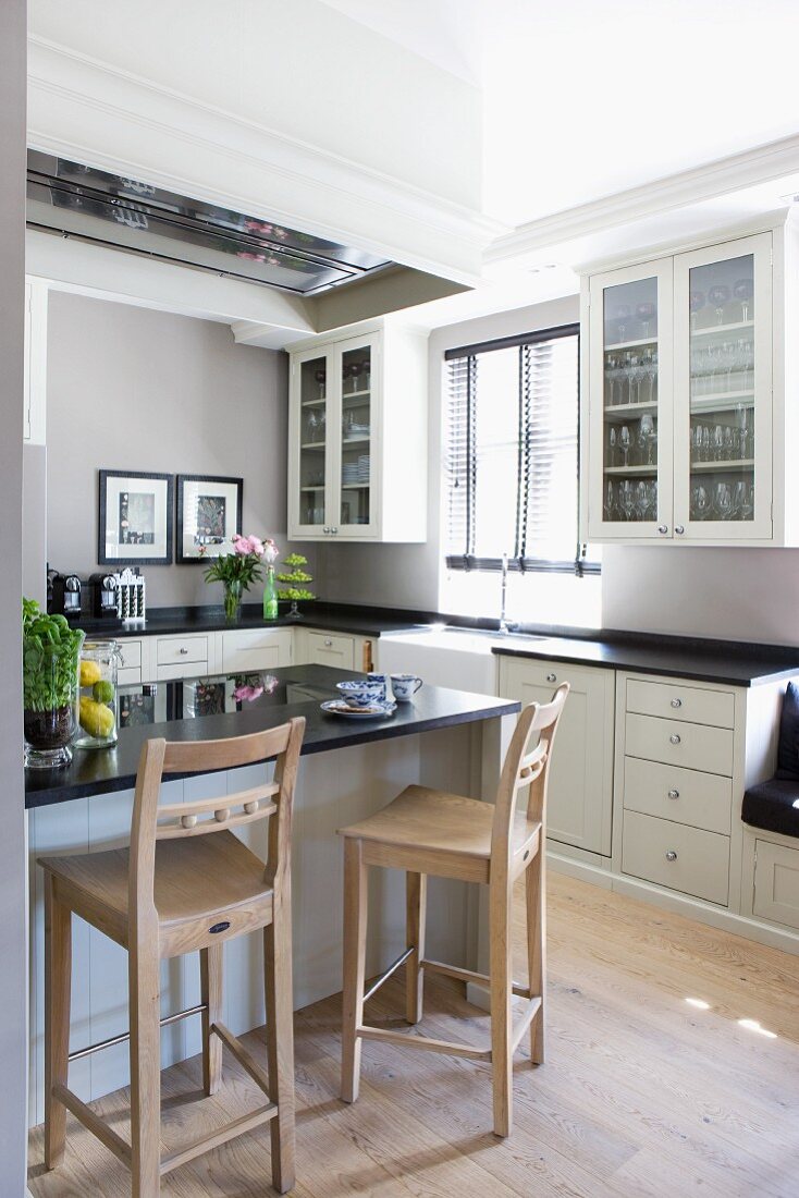 Wooden barstools at counter in white fitted kitchen with black worksurfaces