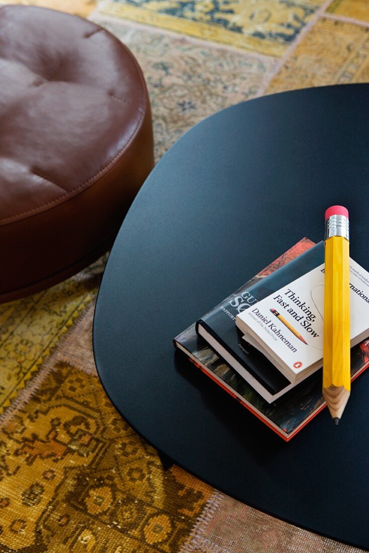 View down onto black metal table and brown leather pouffe on patterned rug