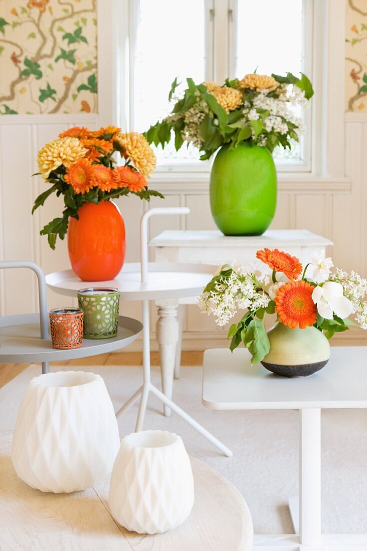 White side tables with bright flower arrangements in vivid green and rich orange