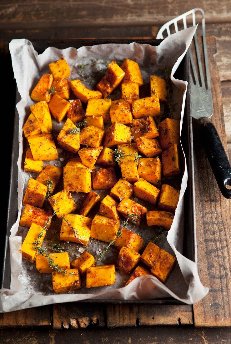 Oven-roasted diced pumpkin with thyme on a baking tray