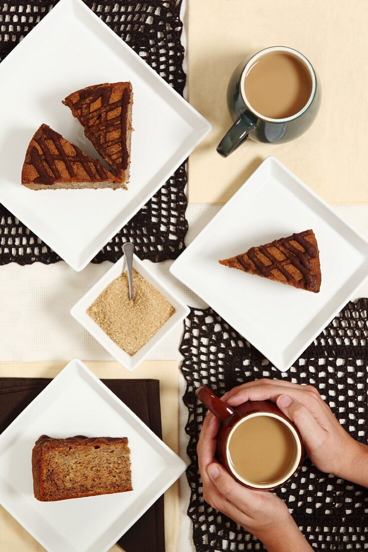 A woman holding a coffee cup surrounded by a few slices of banana & cinnamon cake