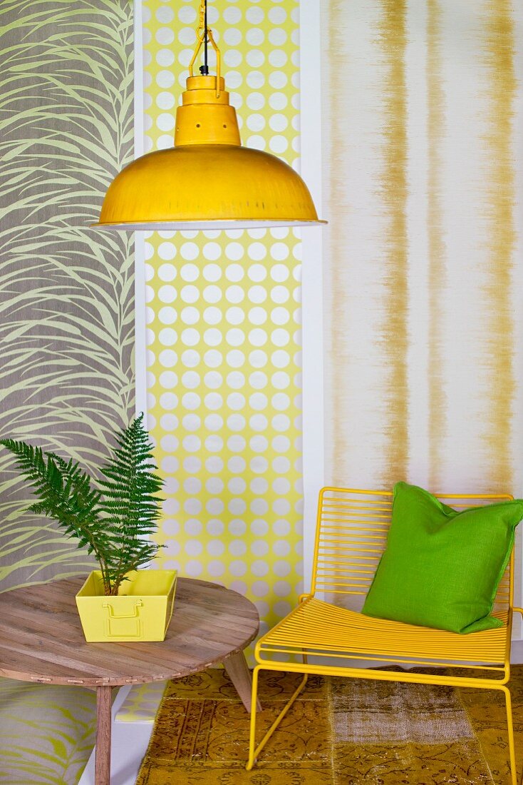 House plant on wooden table, yellow chair and yellow pendant lamp in front of strips of different wallpapers