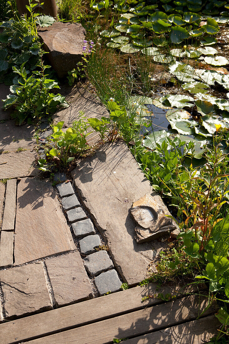 Wooden deck and paved terrace next to lily pond