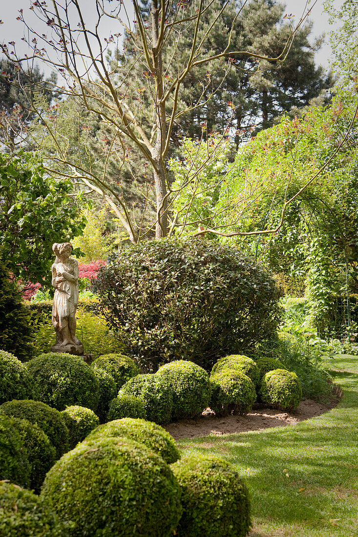 Box balls in front of stone sculpture in manicured garden