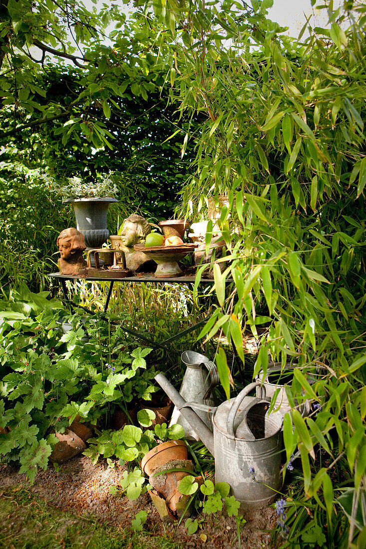 Versteckter Platz mit Blech Giesskannen und Tisch mit Pflanzengefässen im Garten