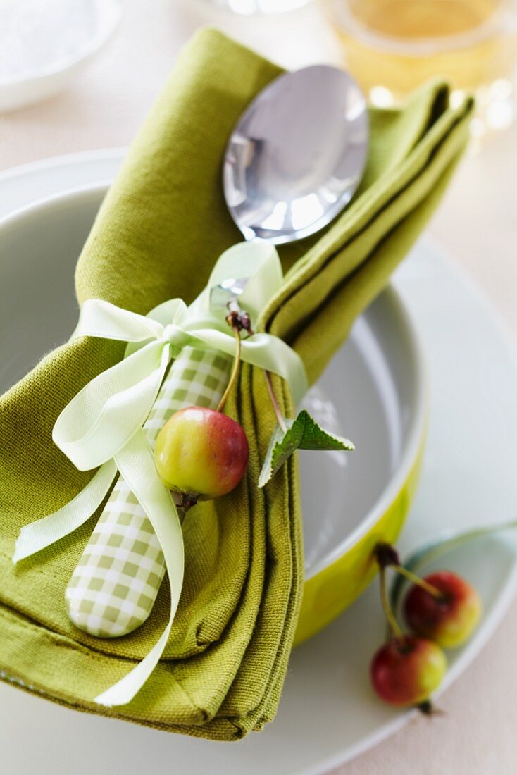 Serviette mit Löffel, zusammengebunden mit Schleifenband und Zieräpfel als Dekoration