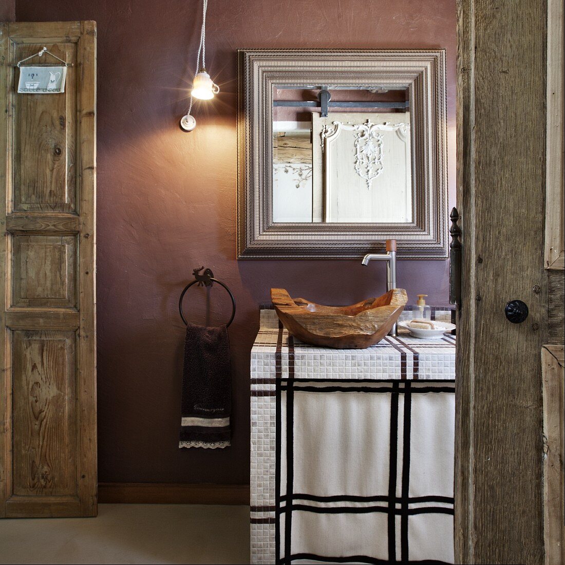 Rustic bathroom with wooden bowl as sink on tiled washstand below mirror on mauve wall