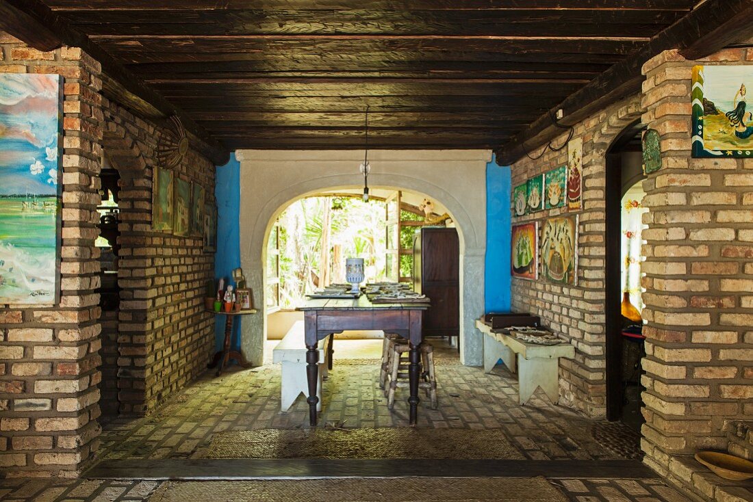 Dining area with colourful religious pictures on brick walls, dark wooden ceiling and rustic wooden furniture