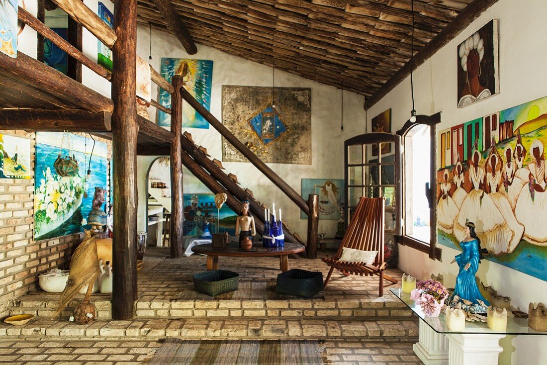 Rustikaler Raum mit Klinkerboden und Galerie aus Rundhölzern; brasilianische Gemälde und Altartische mit Figuren in Blautönen zur Verehrung der Meeresgöttin Lemanja