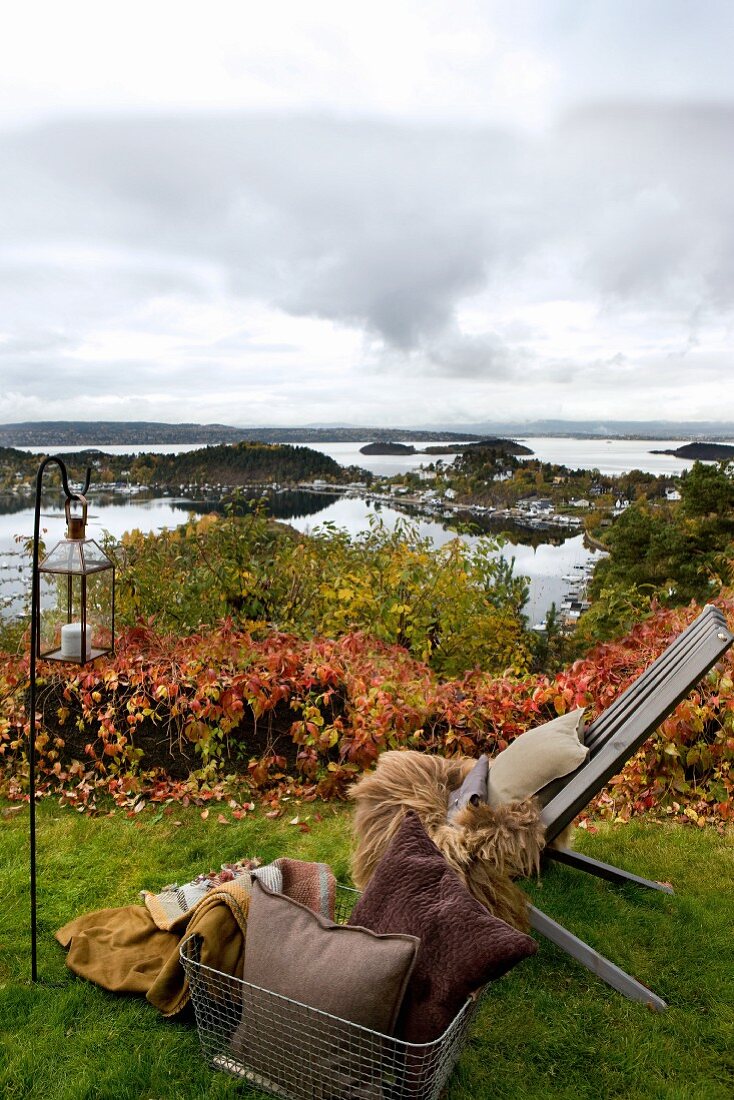 Gartenstuhl mit Felldecken, Kissen und Windlicht in herbstlichem Garten mit Blick auf die norwegische Schärenküsten