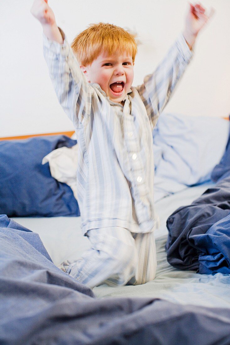 Kleiner Junge mit Rotschopf morgens tobend im Elternbett