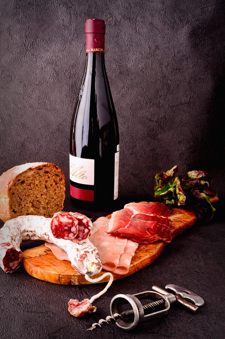 A selection of cold meats with bread, a bottle of red wine and a corkscrew