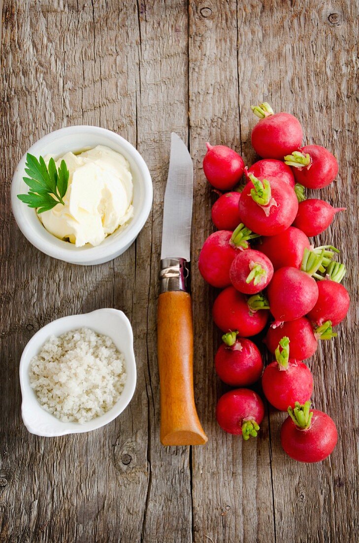 Radieschen mit Salz, Butter und Messer auf Holzuntergrund