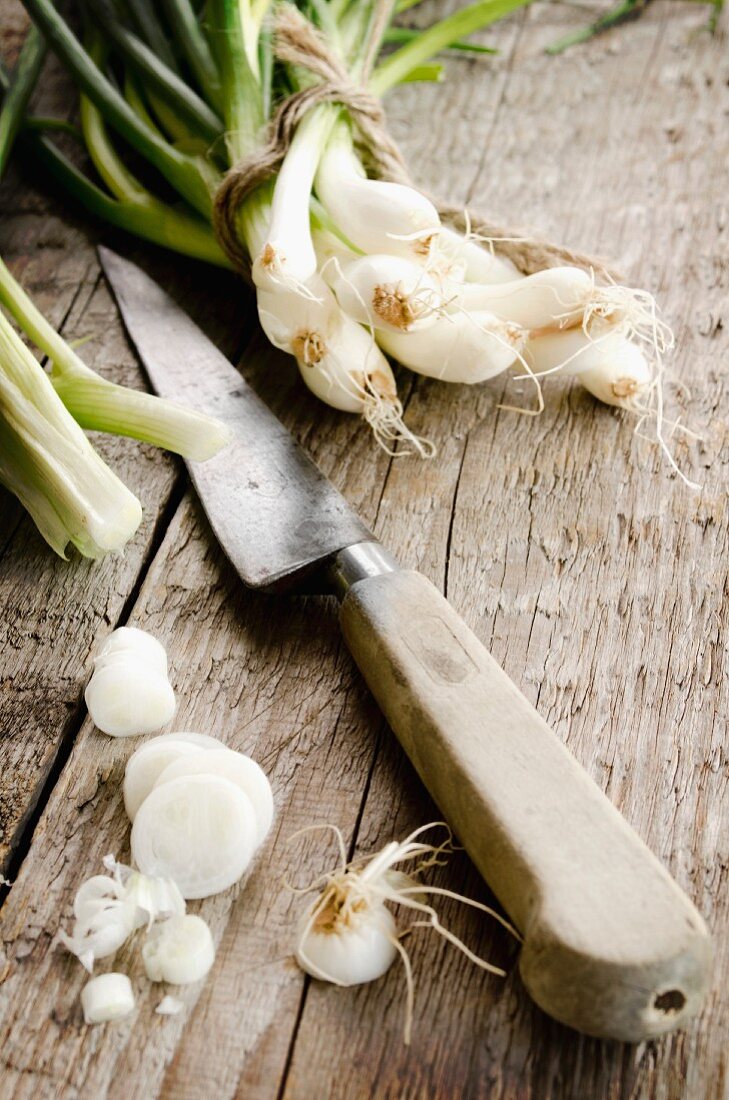 Spring onions, partly slices, with a knife, on a wooden surface