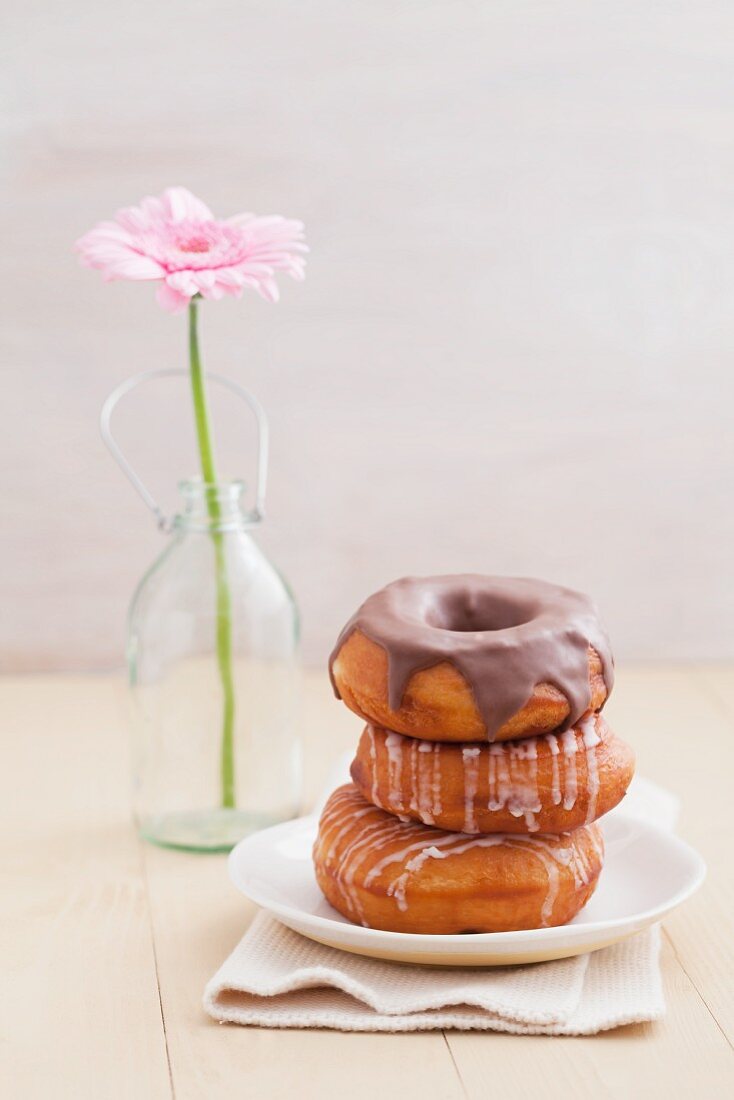 Doughnuts with glacé icing and with chocolate glaze, with a gerbera in the background