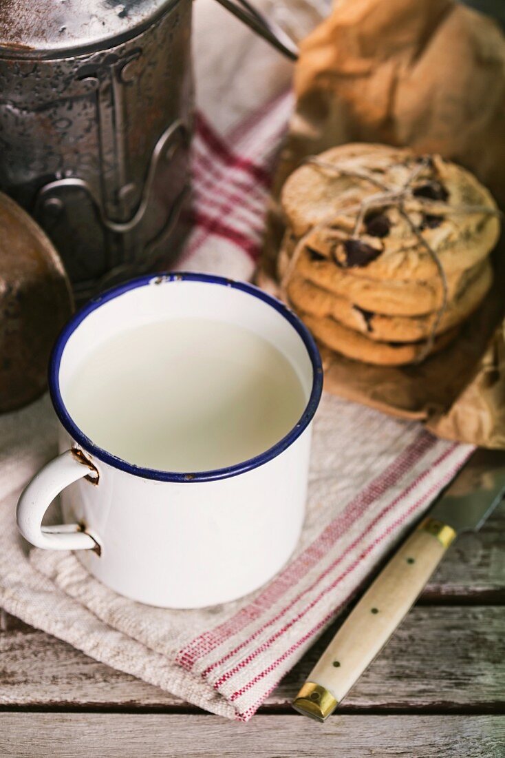 Frische Milch im Emaillebecher und Cookies auf rustikalen Holztisch