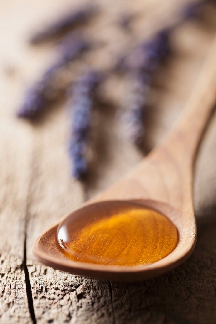 Honey on a wooden spoon, with lavender flowers in the background