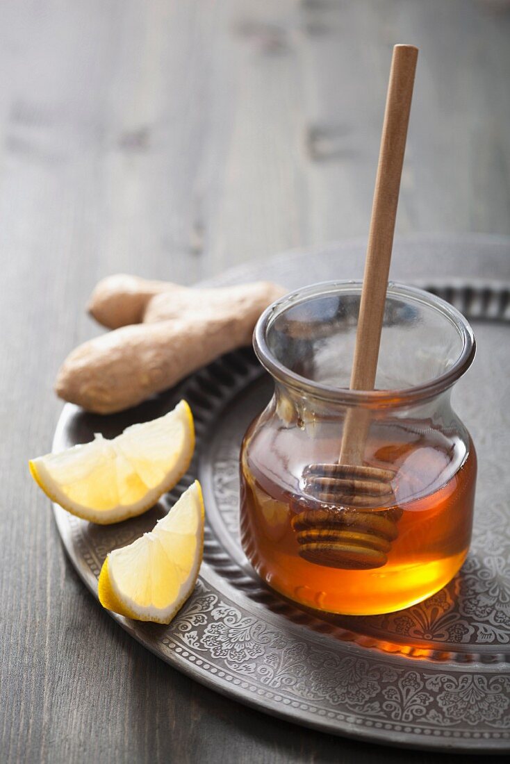 A jar of honey, lemon wedges and ginger