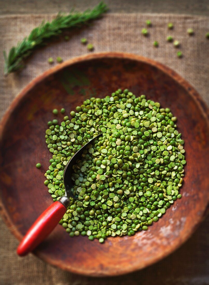 Raw green split peas in an old wooden bowl with an old scoop