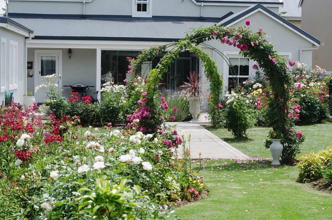 Prachtvoll blühender Garten mit Blumenrabatten und Rosenbögen