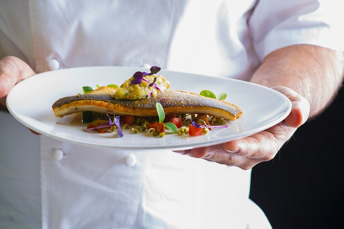 A chef holding a plate of porgy with vegetables and cress