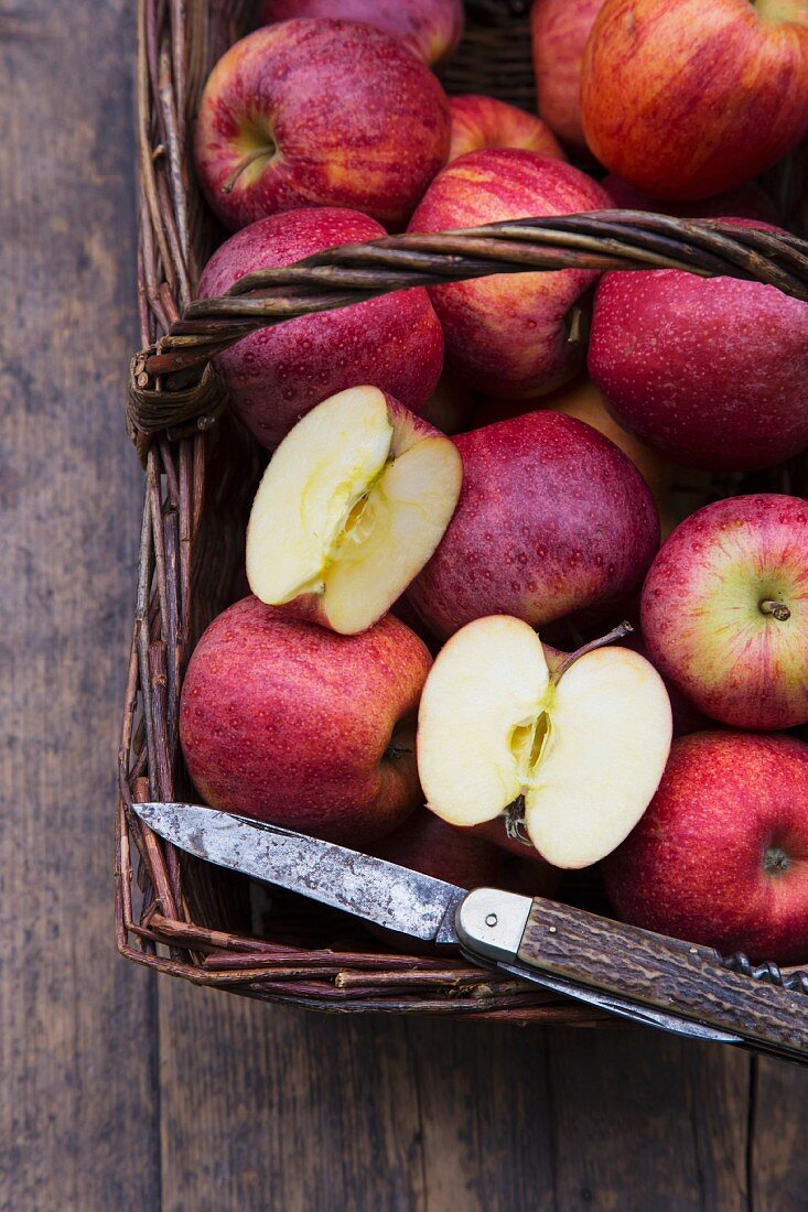 Apples (Royal Gala) in a basket with a knife on a wooden table