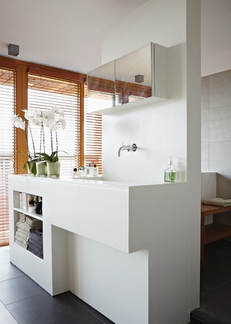 White partition element with sink, surface and shelves in front of glass wall with wooden louver blinds