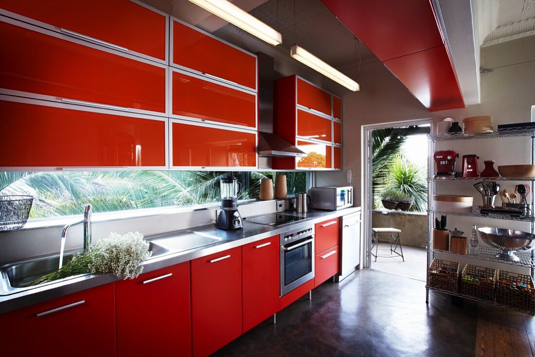 Einbauküche mit roten Fronten und Metallregal neben offener Terrassentür