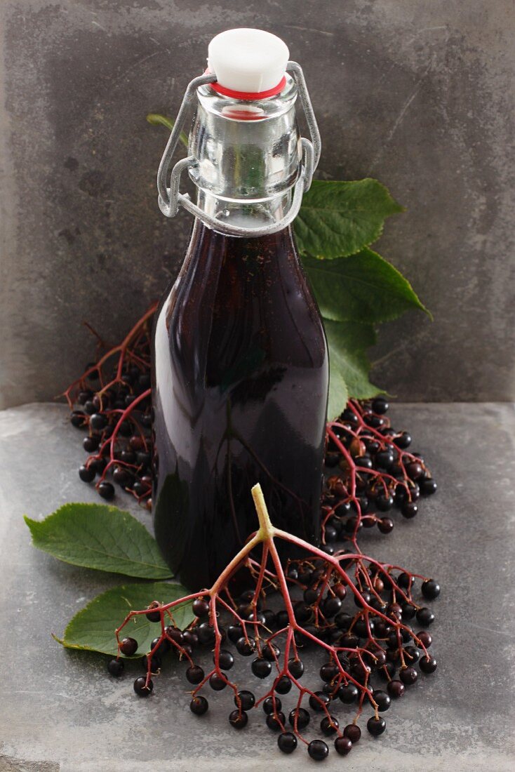 Eine Flasche Holundersaft und frische Holunderbeeren