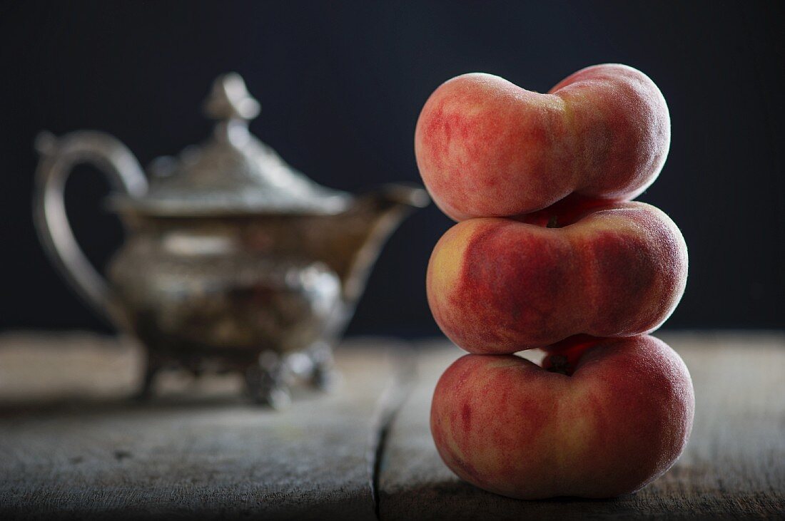 Three stacked vineyard peaches in front of a teapot