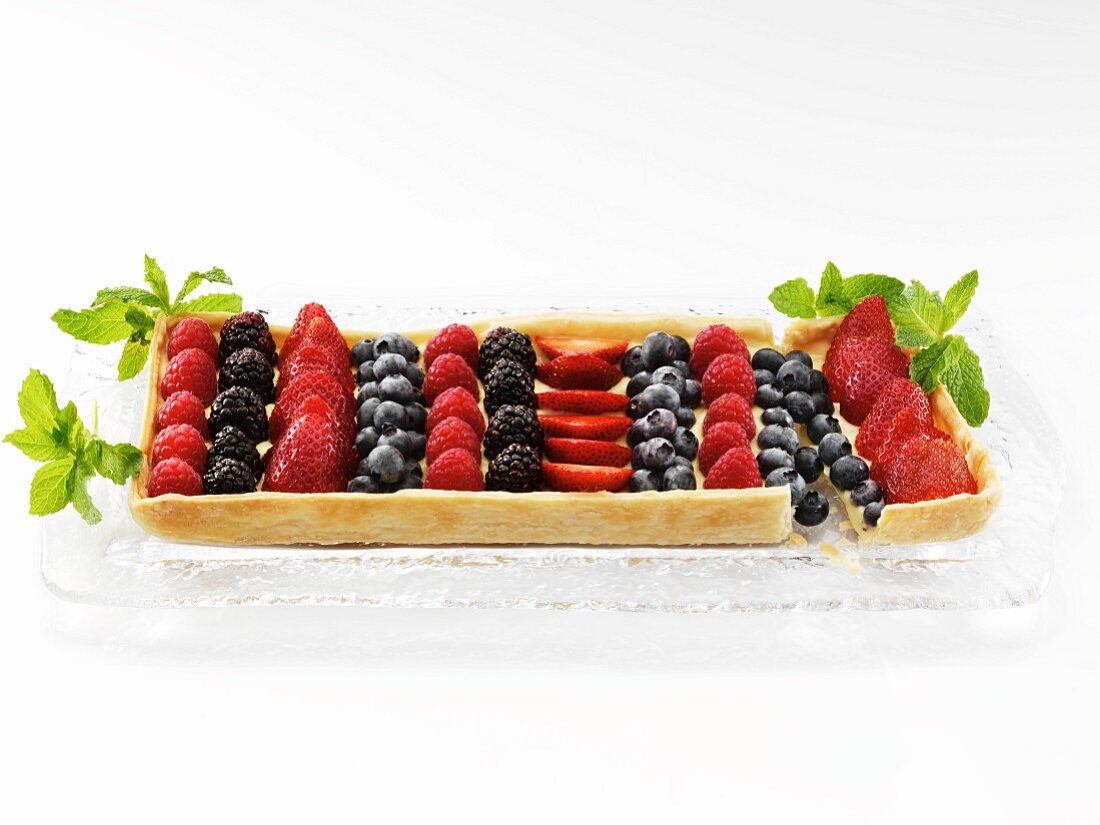 A Rectangular Mixed Berry Fruit Tart on a Glass Tray Garnished with Mint Leaves