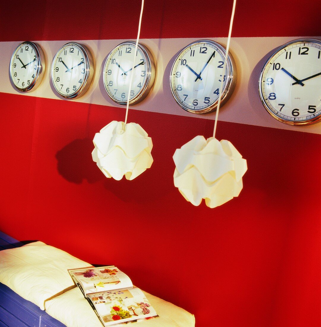 Lamps hanging in front of rows of clocks on red wall