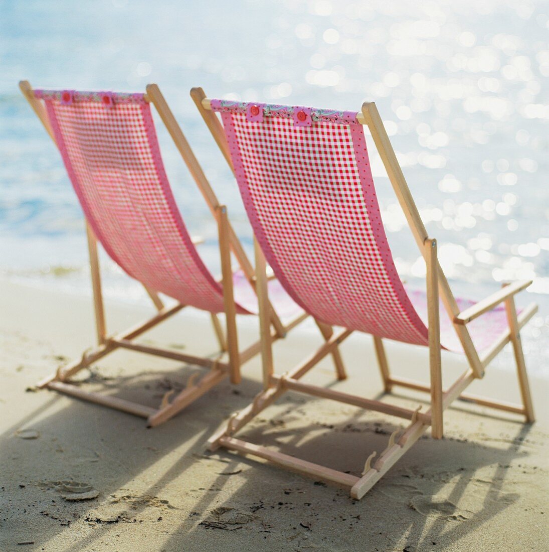 Two sun chairs on a sandy beach.
