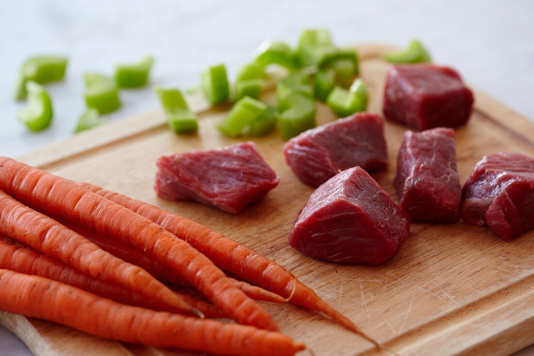 Chunks of Raw Beef, Raw Carrots and Chopped Celery on a Wooden Cutting Board