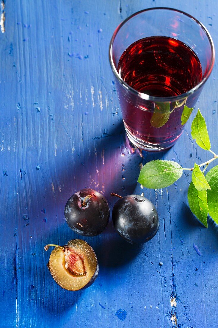 Plums and plum juice on a blue tabletop
