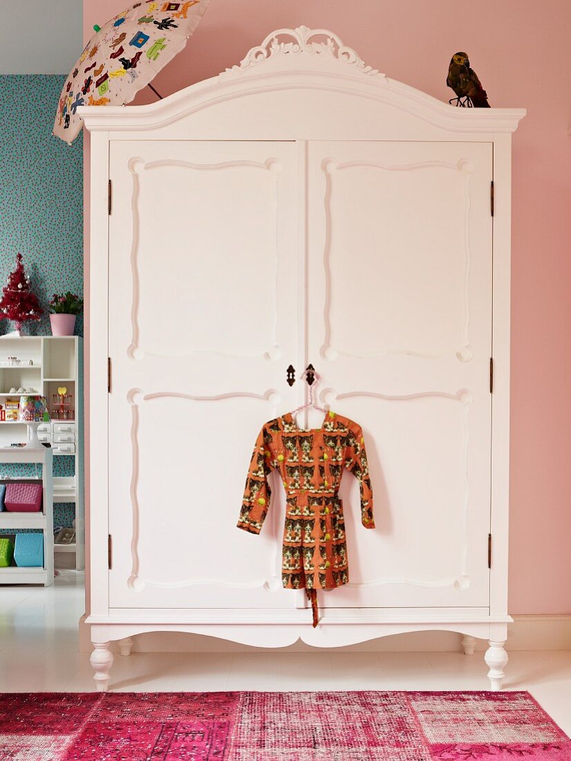 White-painted, antique wardrobe against pink wall in child's bedroom