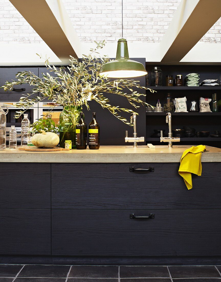 Black kitchen counter with stone top below glass ceiling; bouquet of olive branches on worksurface