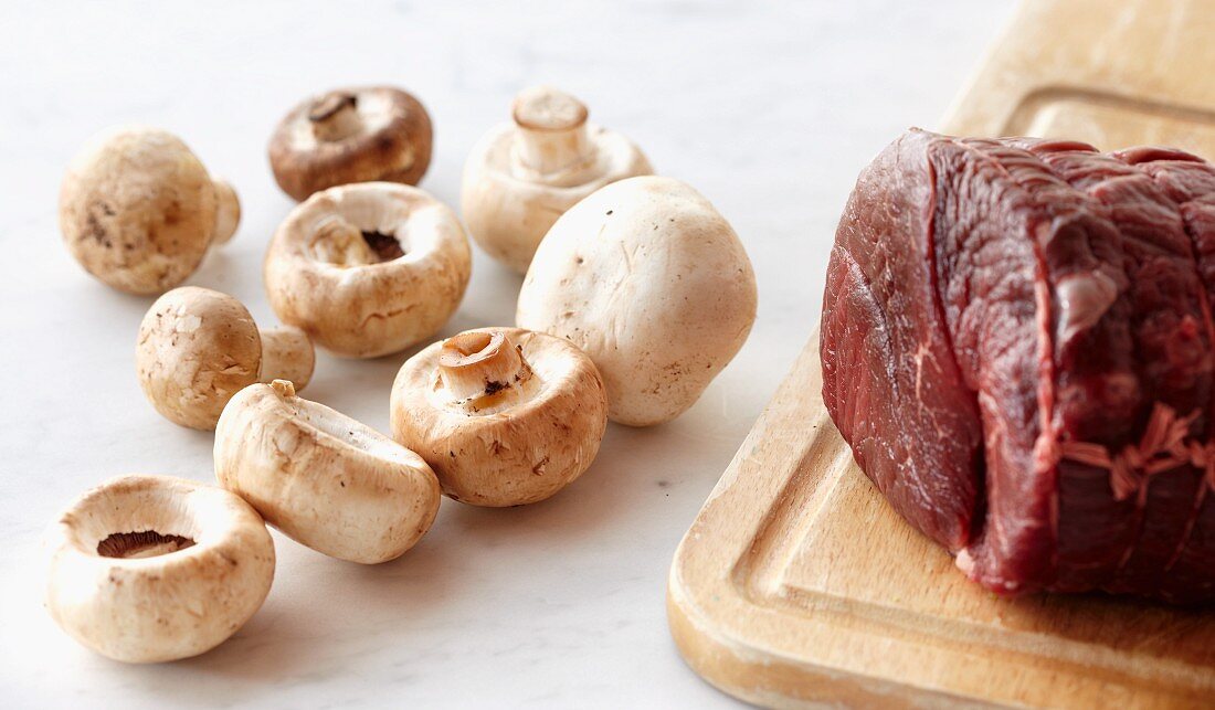 Raw Beef Tenderloin on a Wooden Cutting Board with Raw Mushrooms