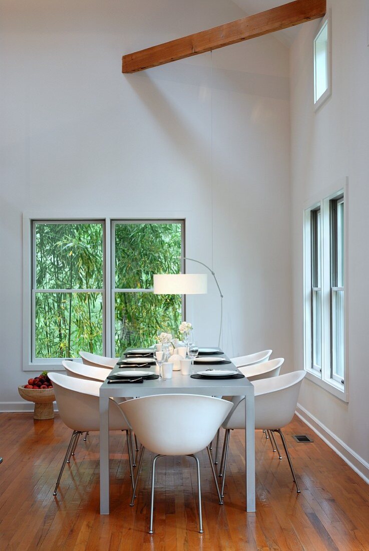 White shell chairs at set table between windows in minimalist dining room