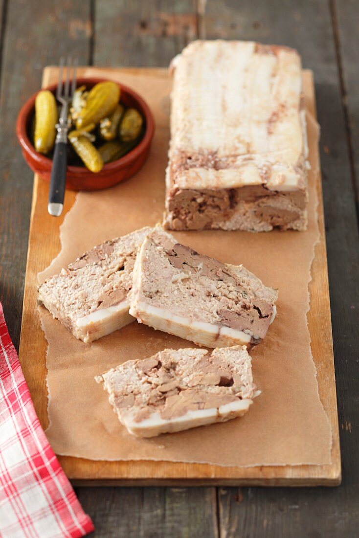 Pâté with chicken liver, partly sliced, and a small bowl of pickled gherkins
