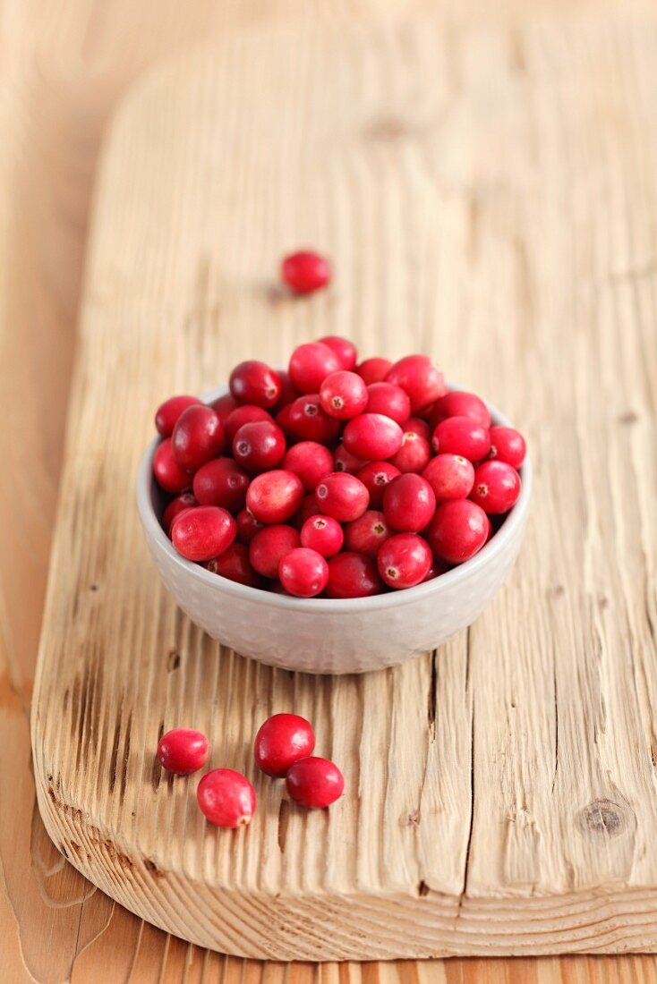Cranberries in a small bowl on a chopping board