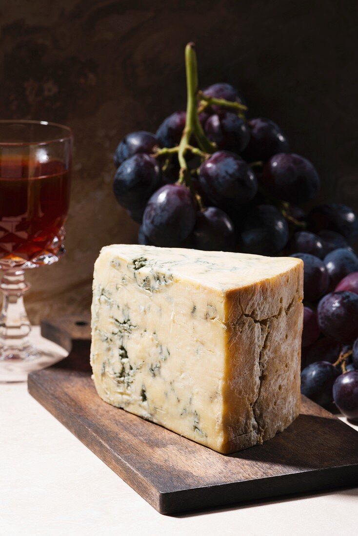 A wedge of blue cheese with grapes and red wine