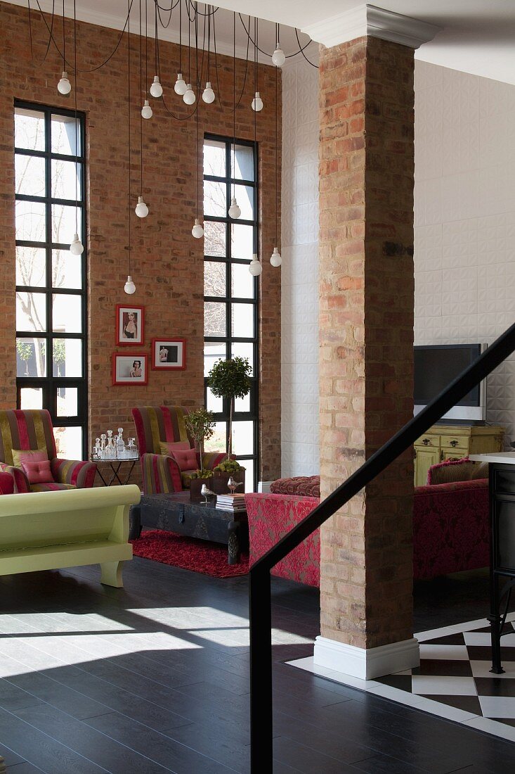 Open-plan interior with free-standing brick pillar in front of lounge area with tall lattice windows; minimalist lamps hanging from ceiling