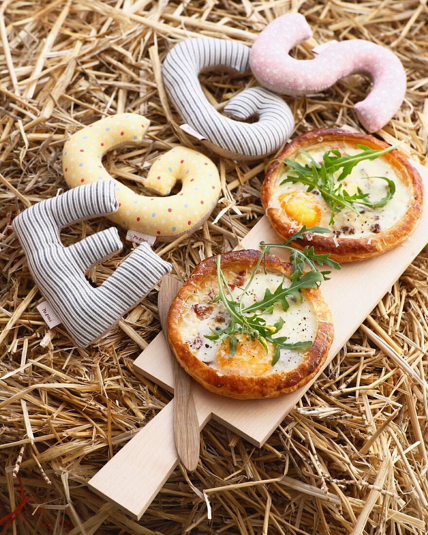 Kleine Specktartes mit Spiegelei und Rucola auf Schneidebrett im Stroh