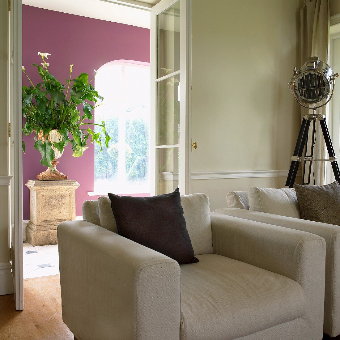 Two armchairs in interior; urn of flowers on stone pedestal against deep violet wall in background