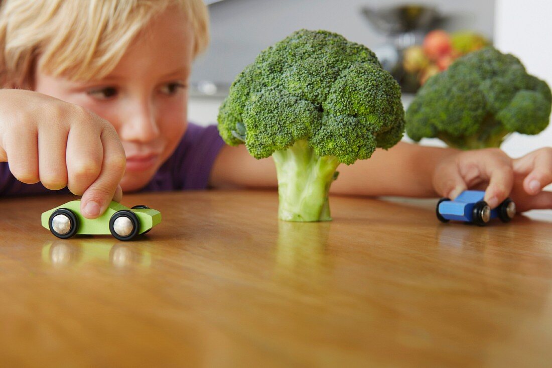 Boy playing cars around broccoli trees