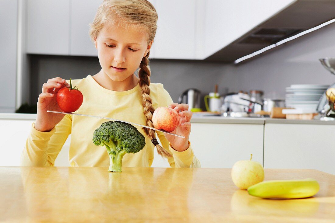 Mädchen balanciert Apfel und Tomate auf einer Brokkoli-Waage